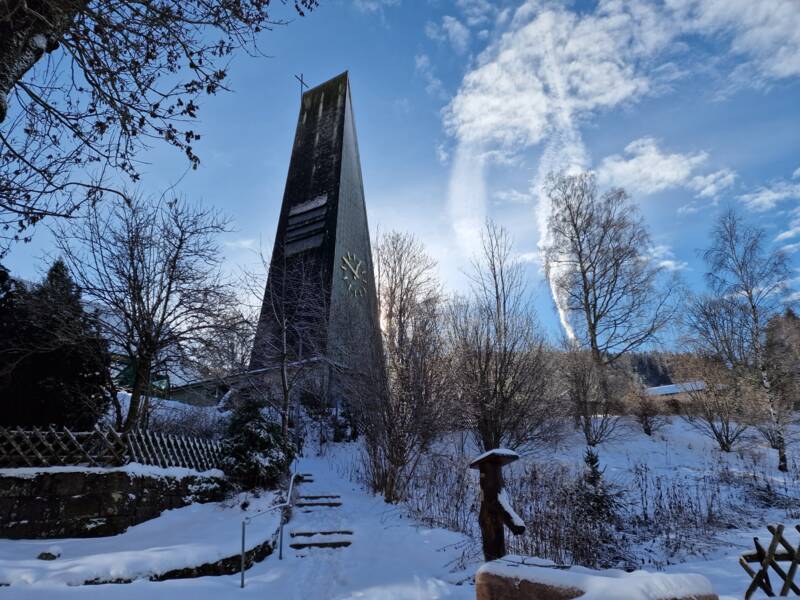 Dreieckige hohe grünfarbende Kirche im Dorf mit Brunnen auf dem Vorplatz