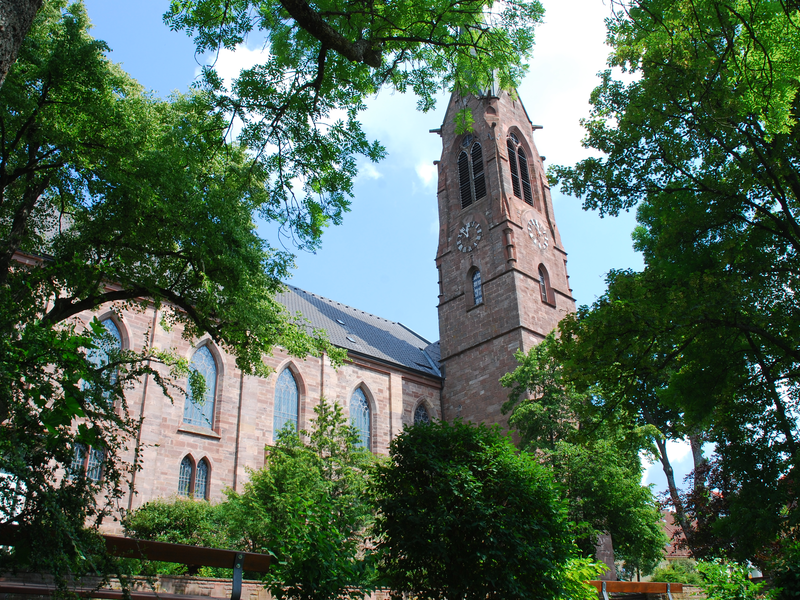 Kirche mit Turm aus Sandstein und grünen Bäumen im Vordergrund