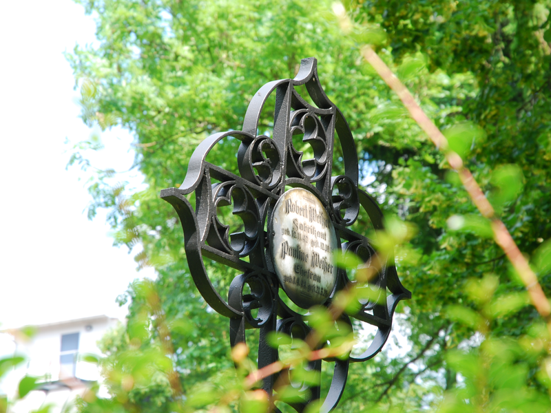 Eisernes Grabkreuz vor grünem Baum