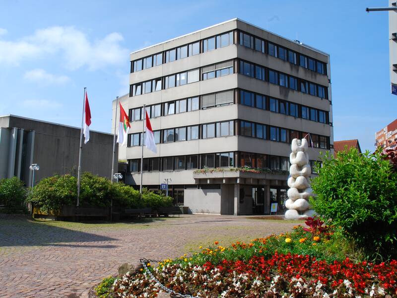 Rathaus St. Georgen: Rechteckiges Betongebäude mit Brunnen und Beflaggung vor der Eingangstüre